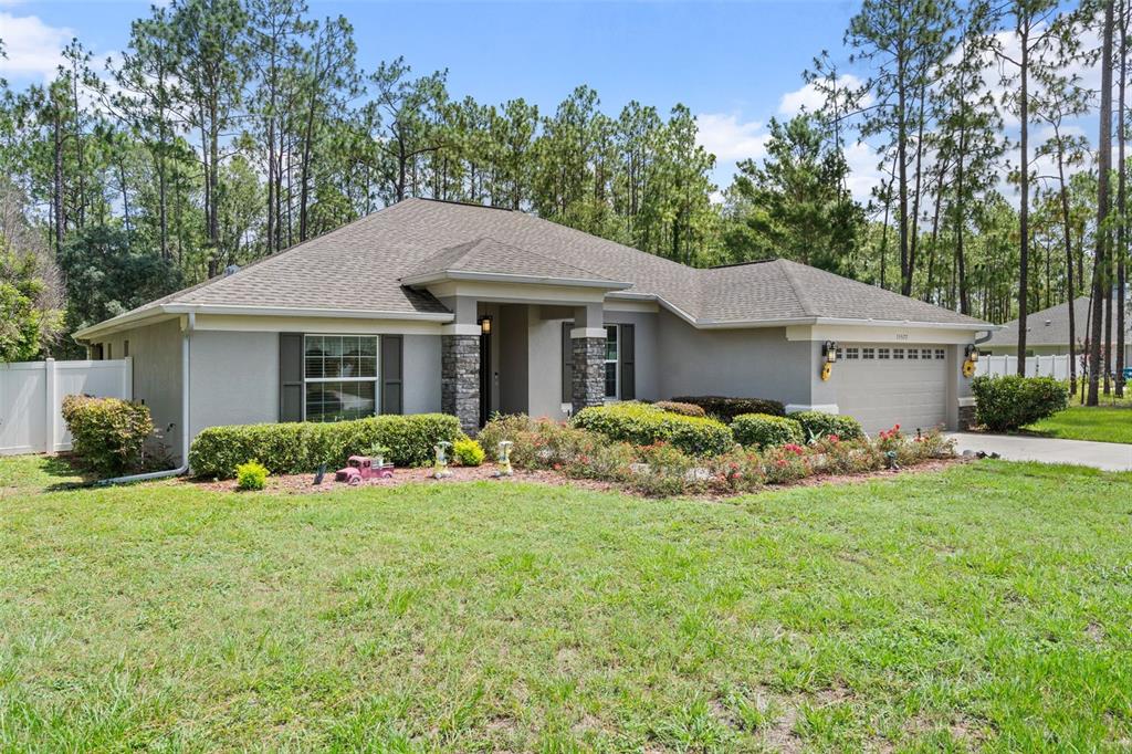 A single-story suburban house with a gray stucco exterior, stone columns, and a two-car garage — 15577 SAGO DRIVE, BROOKSVILLE, FL