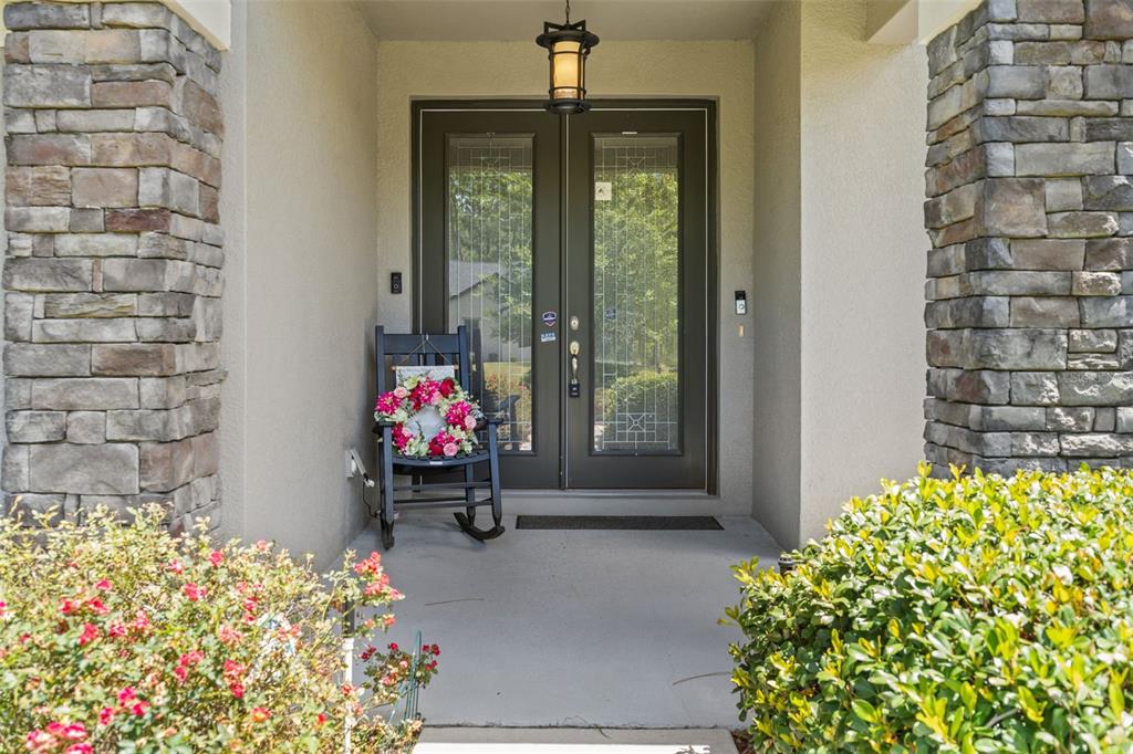 A front porch features a black rocking chair, double glass doors, and stone pillars — 15577 SAGO DRIVE, BROOKSVILLE, FL