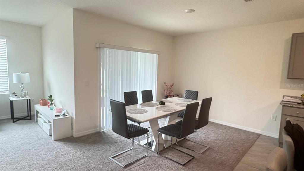 A dining area features a white table with six black chairs on carpeted flooring — 2175 DOE RUN DRIVE, DAVENPORT, FL