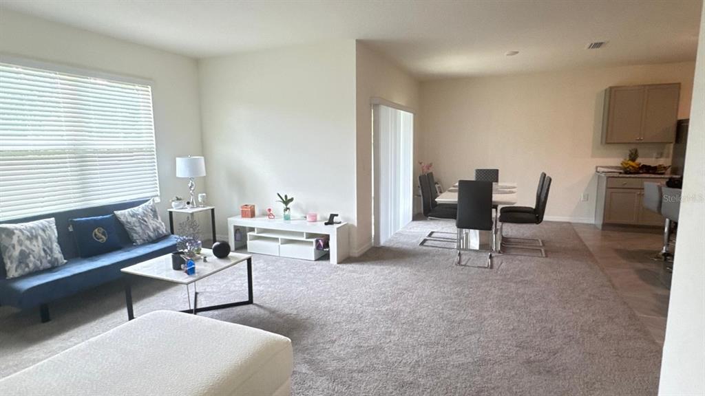An open-concept living and dining area features carpeted flooring, a blue sofa, and kitchen cabinetry — 2175 DOE RUN DRIVE, DAVENPORT, FL