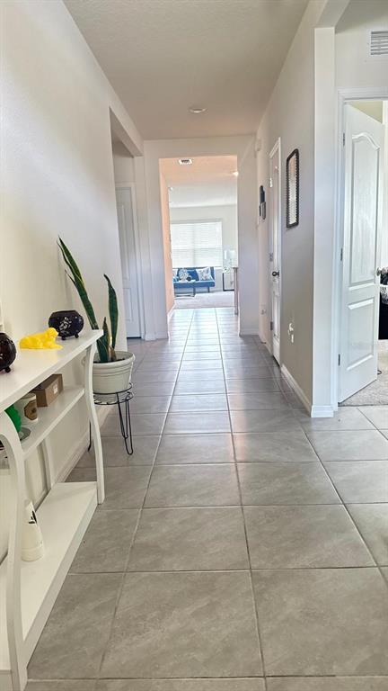 A hallway with light-colored tile flooring leads toward a living area with a blue sofa — 2175 DOE RUN DRIVE, DAVENPORT, FL