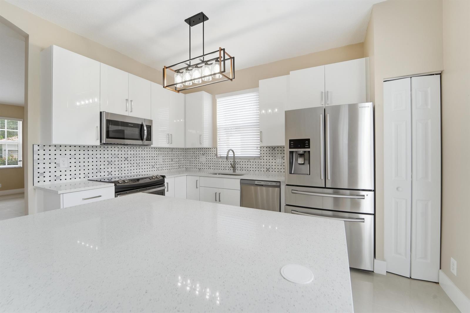 A modern kitchen features white cabinets, stainless steel appliances, a quartz island, and patterned backsplash — 1780 Pierside Circle, Wellington FL 33414, WELLINGTON, FL