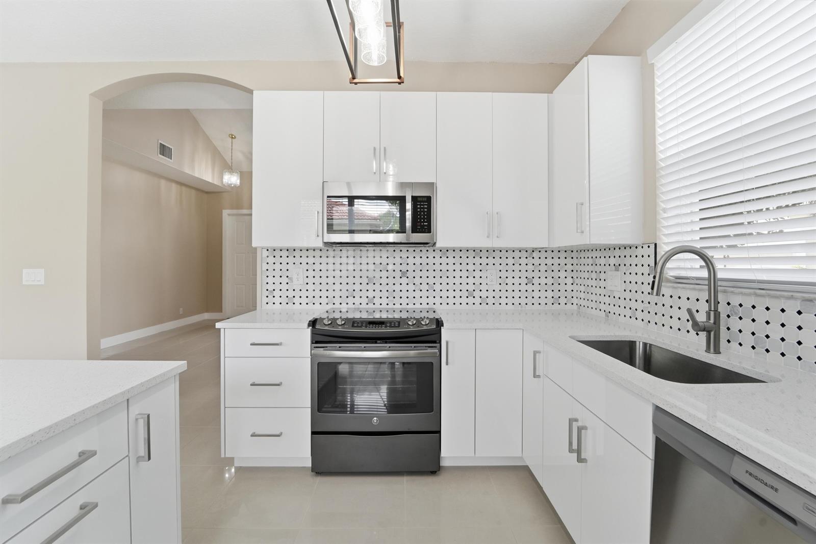A modern kitchen features white cabinets, a black stove, a patterned backsplash, and quartz countertops — 1780 Pierside Circle, Wellington FL 33414, WELLINGTON, FL