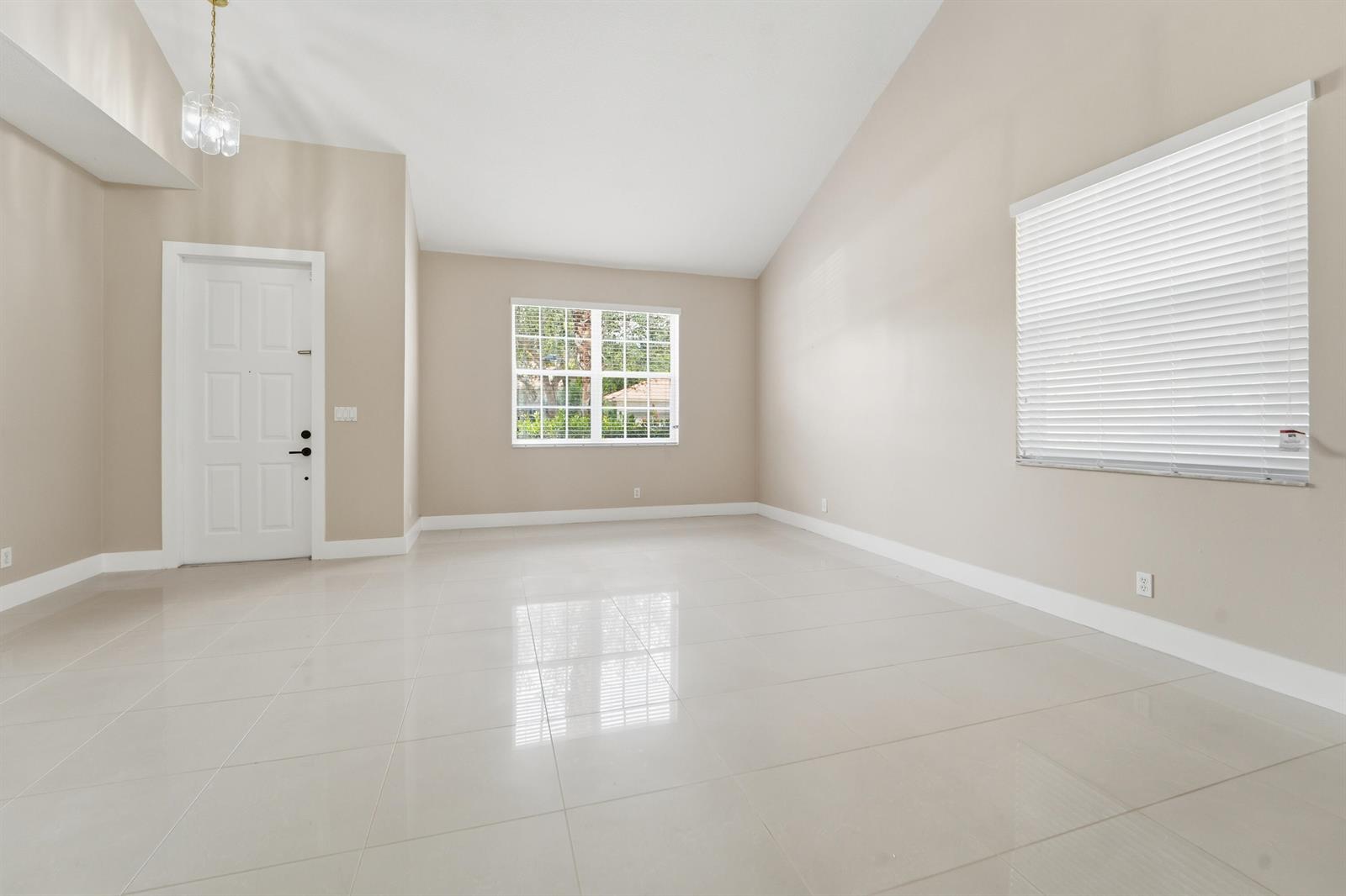 An empty room with beige walls, white tile flooring, a vaulted ceiling, and two windows — 1780 Pierside Circle, Wellington FL 33414, WELLINGTON, FL