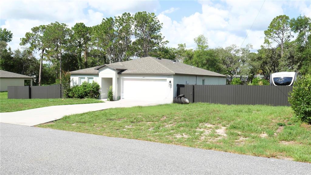A single-story house with a white garage, gray roof, and a dark metal fence — 12150 FOLGER STREET, SPRING HILL, FL