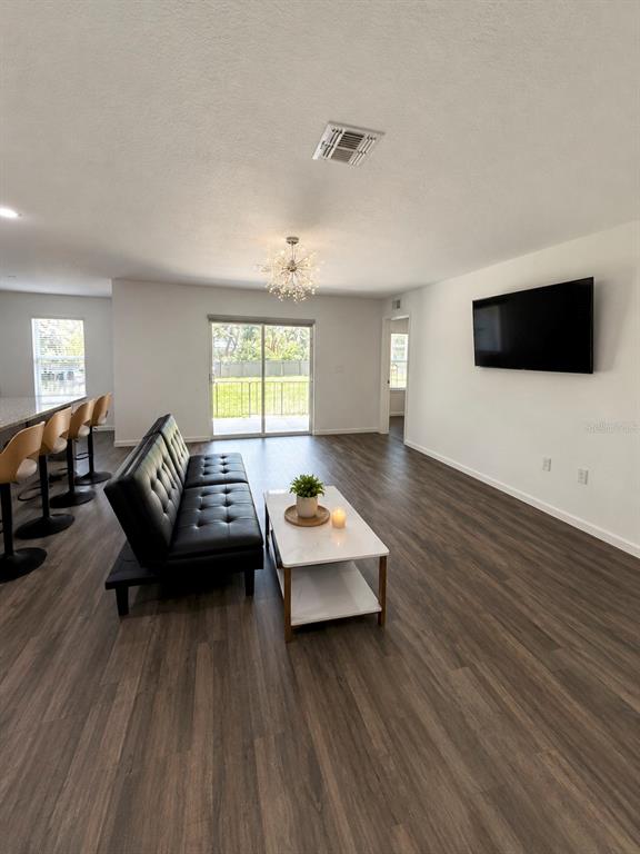 A living room features wood-look flooring, a black futon, a coffee table, and a wall-mounted television — 12150 FOLGER STREET, SPRING HILL, FL