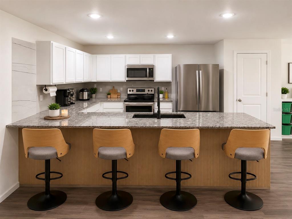A kitchen features white cabinets, granite countertops, a breakfast bar with four stools, and appliances — 12150 FOLGER STREET, SPRING HILL, FL