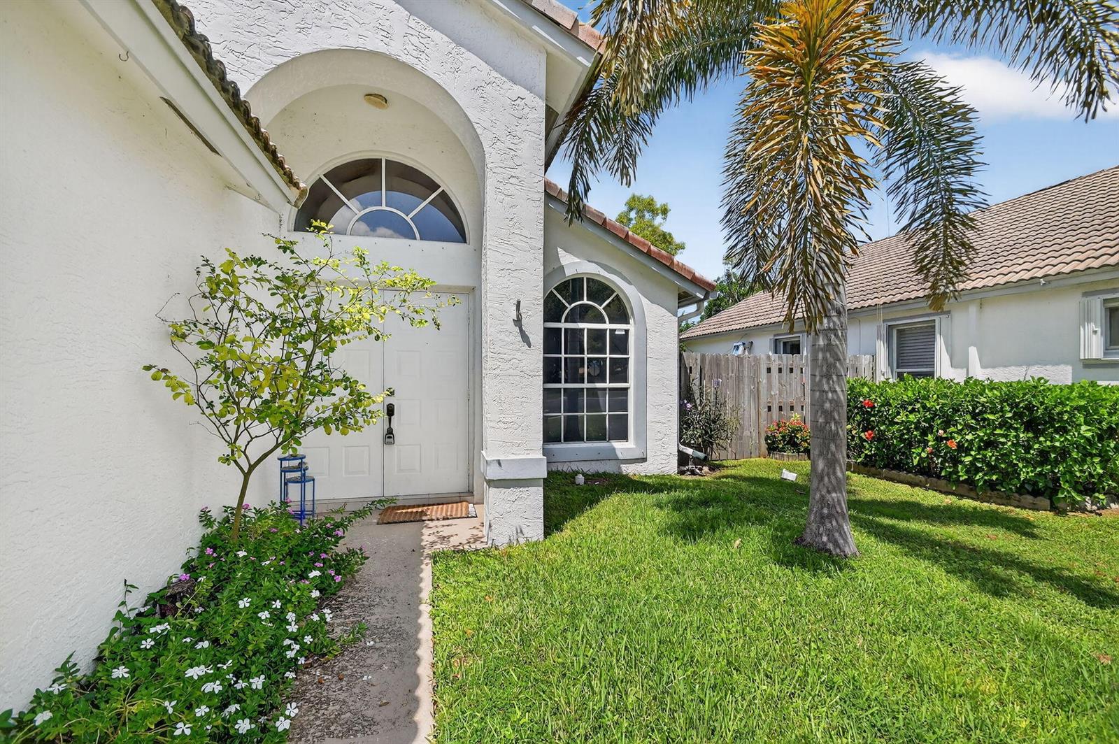 A white house exterior features a double front door, arched windows, and a palm tree — 1891 Oak Berry Circle, Wellington FL 33414, WELLINGTON, FL