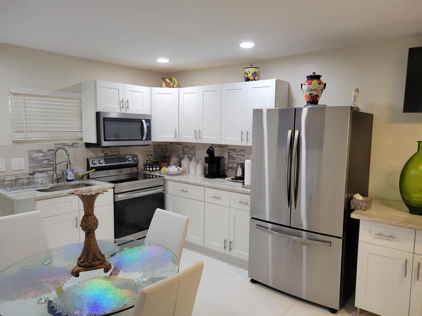 A kitchen features white cabinets, stainless steel appliances, a glass dining table, and tile flooring — 3124 NE Skyline Drive # B, Jensen Beach FL 34957, JENSEN BEACH, FL