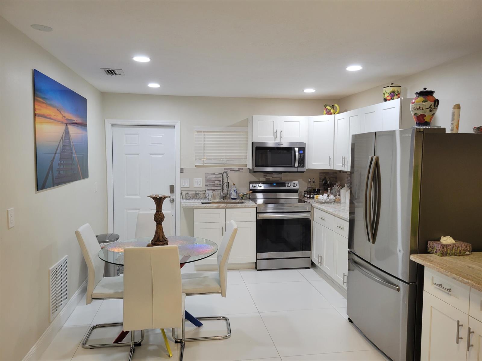 A kitchen with white cabinets, stainless steel appliances, a glass dining table, and tile floors — 3124 NE Skyline Drive # B, Jensen Beach FL 34957, JENSEN BEACH, FL