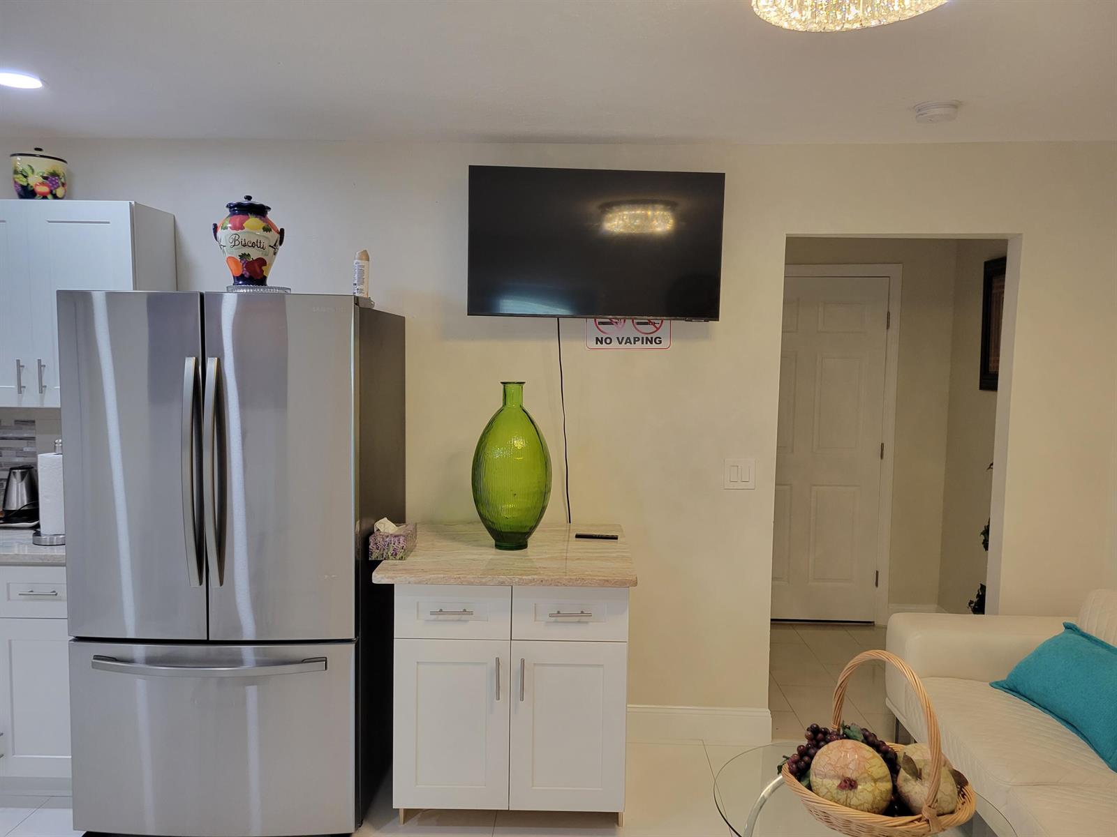 A kitchen area features a stainless steel refrigerator, a white cabinet, and a wall-mounted television — 3124 NE Skyline Drive # B, Jensen Beach FL 34957, JENSEN BEACH, FL