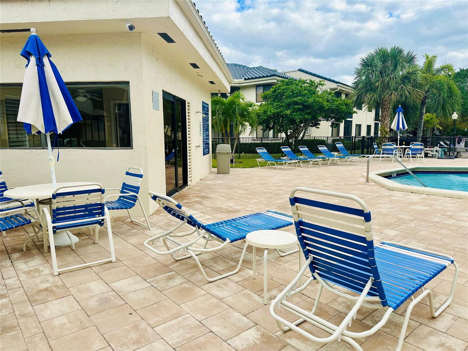 A pool deck with blue and white lounge chairs, tables, and umbrellas near a building — 8142 NW 17th Manor, Plantation FL 33322, PLANTATION, FL