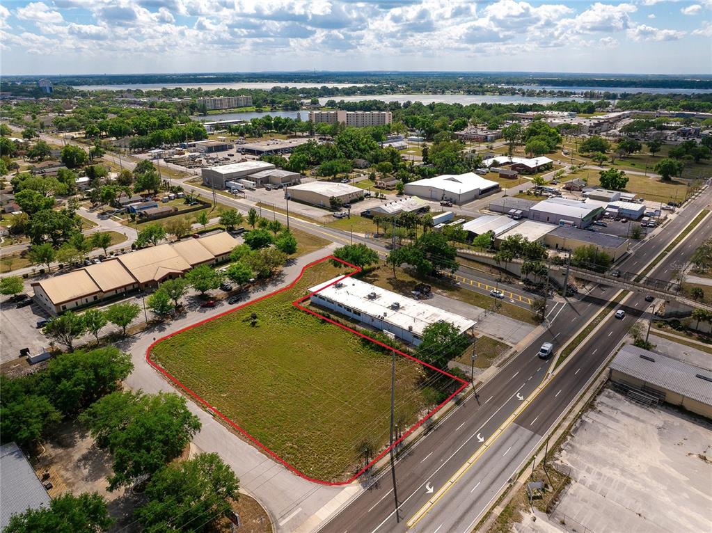 An aerial view shows a vacant, grass-covered commercial lot outlined in red next to a building — 0 OLYMPIAN WAY, WINTER HAVEN, FL