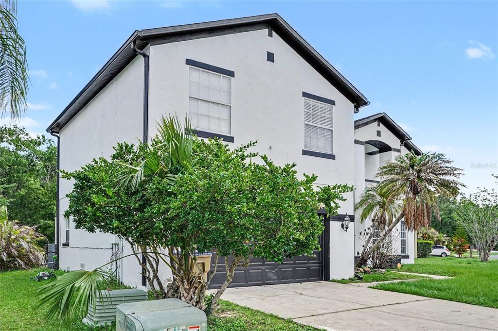 A two-story white stucco house with a dark garage door and a large front tree — 5385 DAHLIA RESERVE DRIVE, KISSIMMEE, FL