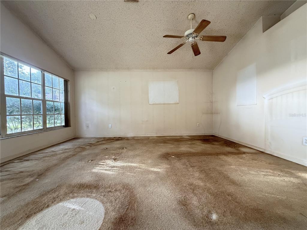 An empty room features a ceiling fan, large windows, and heavily stained wall-to-wall carpeting — 6608 NORTHHAVEN COURT, RIVERVIEW, FL