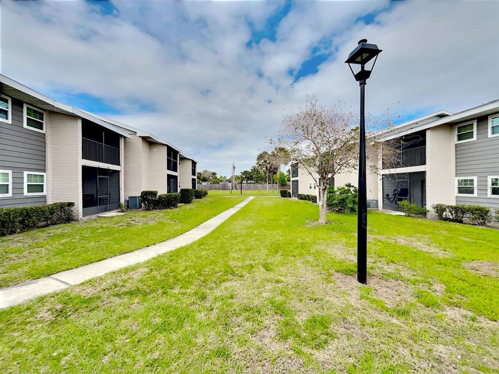 A grassy courtyard sits between two multi-story apartment buildings with a central walkway and lamp — 865 SKY LAKE CIRCLE UNIT D, ORLANDO, FL