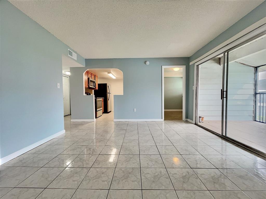 A living area with light blue walls, tiled floors, a kitchen pass-through, and sliding doors — 865 SKY LAKE CIRCLE UNIT D, ORLANDO, FL