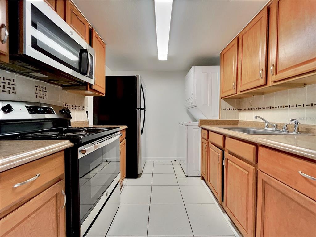 A galley kitchen features wood cabinets, a black stove, a black refrigerator, and white tile floors — 865 SKY LAKE CIRCLE UNIT D, ORLANDO, FL
