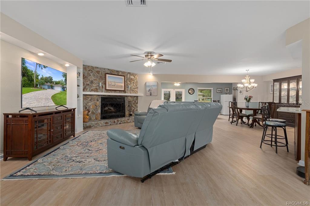 A living room with a stone fireplace, light wood flooring, and an adjacent dining area — 11678 W TIMBERLANE DRIVE, HOMOSASSA, FL