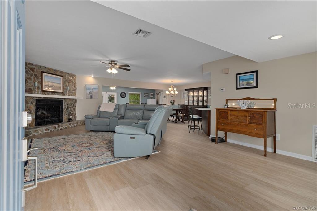 A living room with a stone fireplace, light wood flooring, and an open dining area — 11678 W TIMBERLANE DRIVE, HOMOSASSA, FL