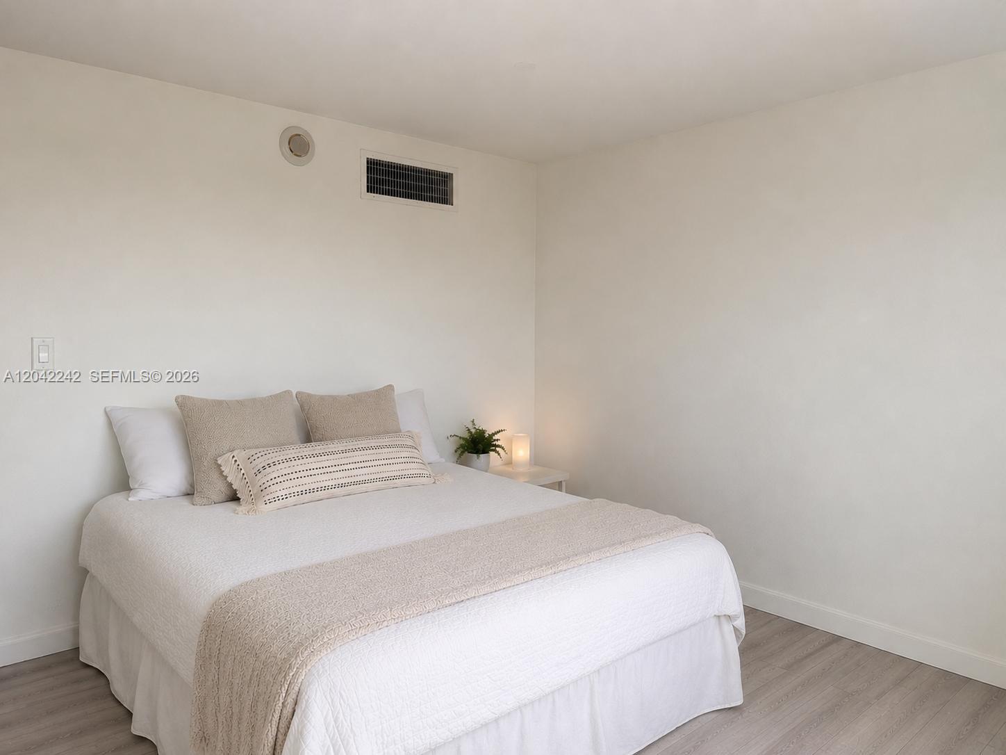 A bedroom features a bed with neutral bedding, light wood flooring, and white walls — 10275 Collins Ave # 431, Bal Harbour FL 33154, BAL HARBOUR, FL
