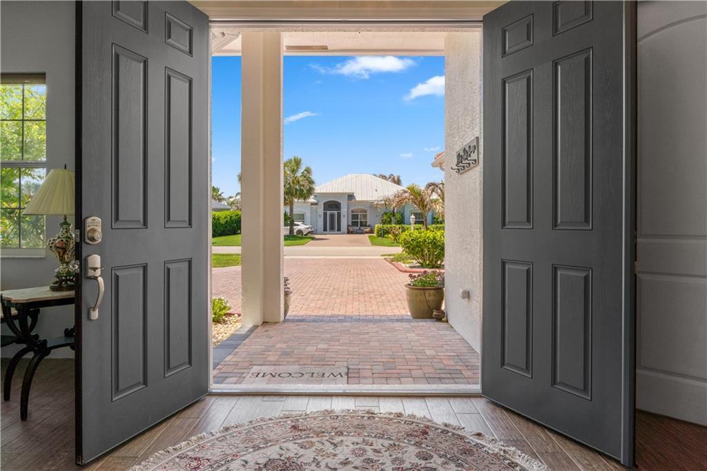A view through an open double door looking out onto a brick-paved driveway and house — SEBASTIAN, FL