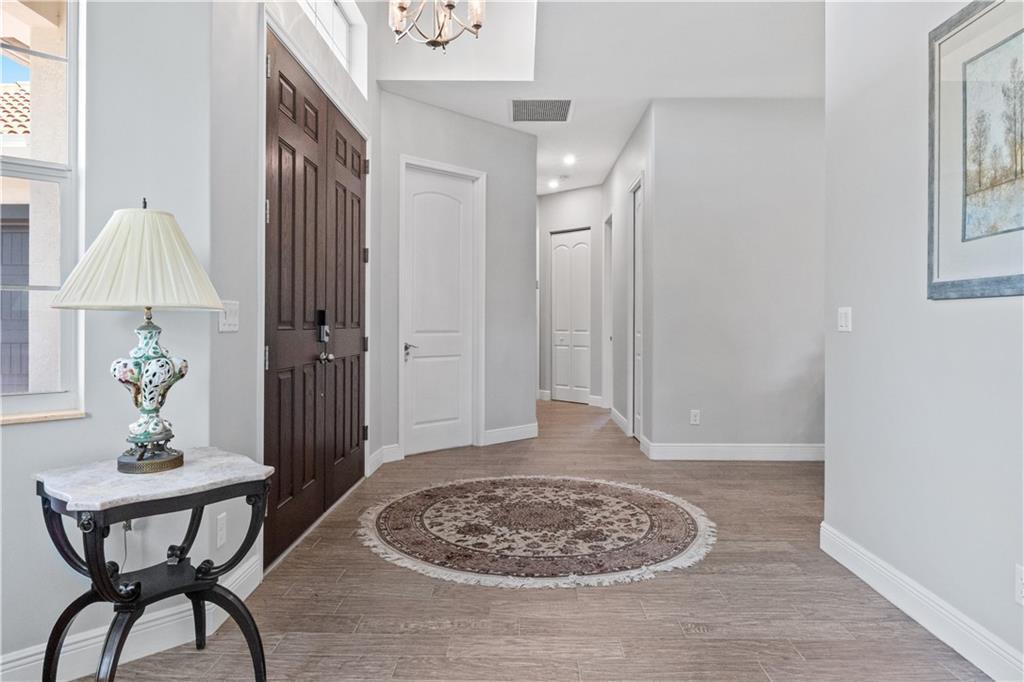 A bright foyer features light wood-look tile flooring, a round rug, and a dark door — SEBASTIAN, FL
