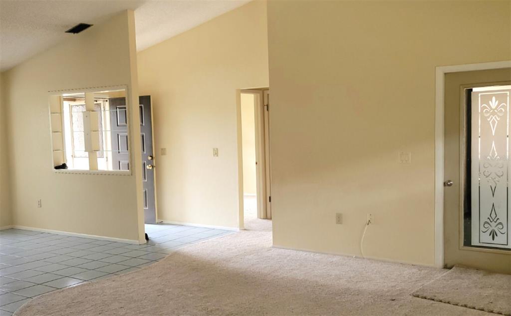 A living room with beige carpet, light-colored walls, and a doorway with a decorative glass insert — 11306 POSSUM TRAIL, PORT RICHEY, FL