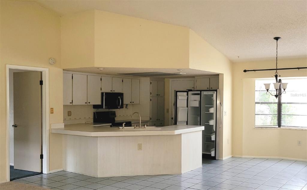 A kitchen with white cabinets, a peninsula counter, and tile flooring opens to a dining area — 11306 POSSUM TRAIL, PORT RICHEY, FL