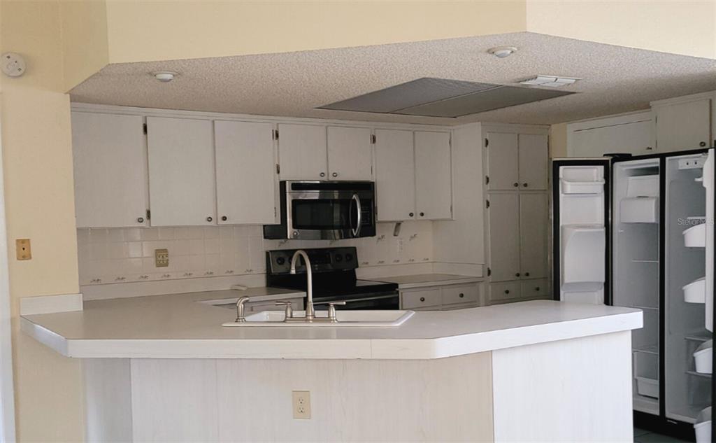 A kitchen features white cabinets, a microwave, a sink, and a refrigerator with an open door — 11306 POSSUM TRAIL, PORT RICHEY, FL