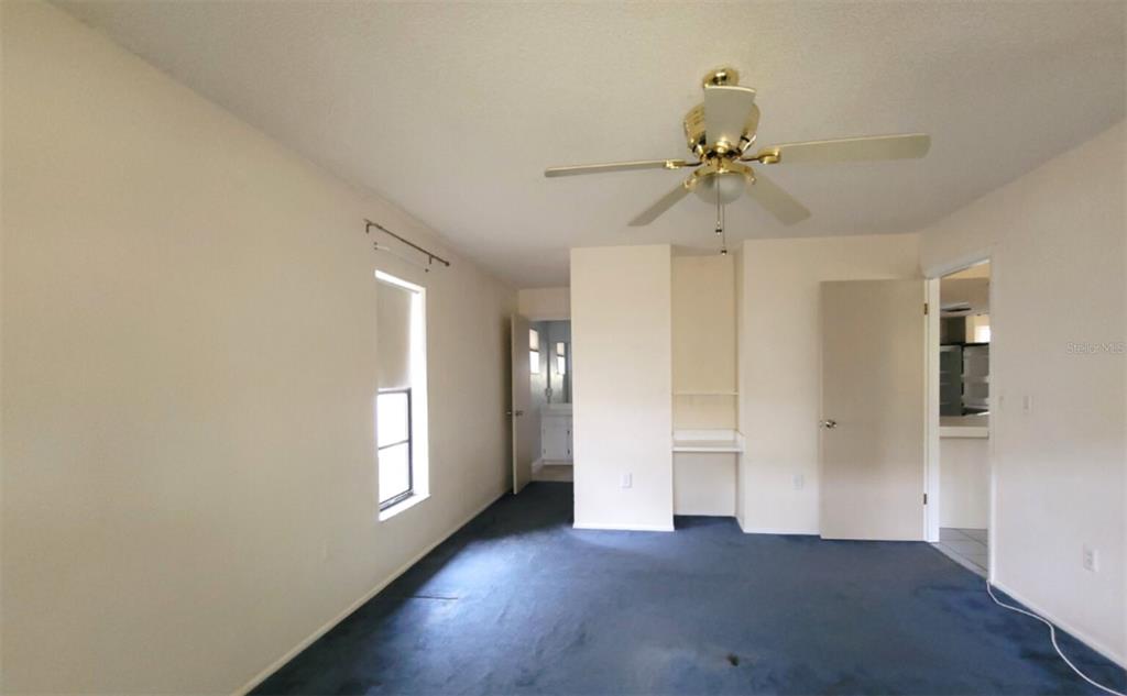 A bedroom features blue carpeting, a ceiling fan, a built-in desk, and an attached bathroom — 11306 POSSUM TRAIL, PORT RICHEY, FL