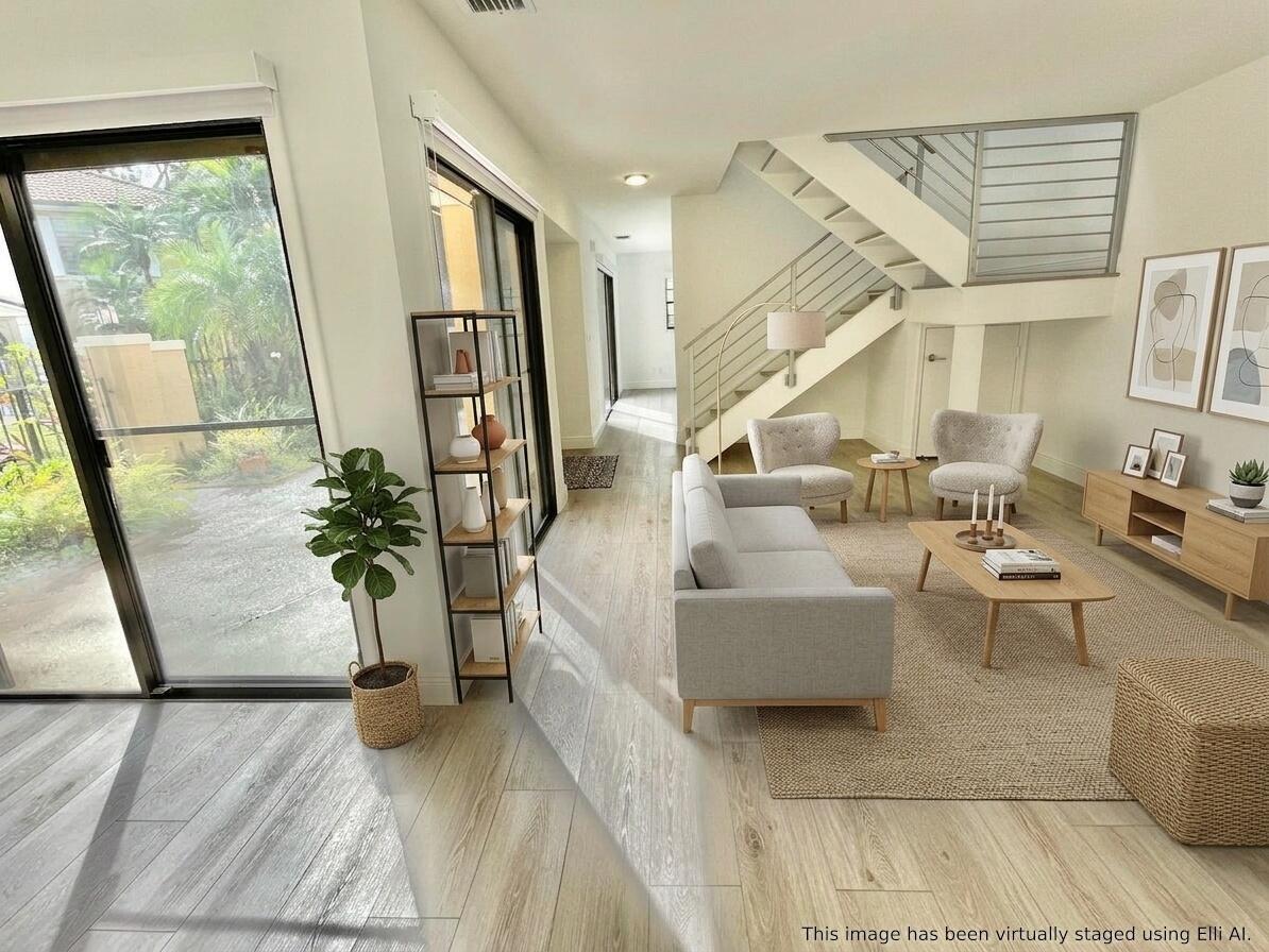 This virtually staged living room features light wood flooring, a staircase, and sliding glass doors — 359 Prestwick Circle # 2, Palm Beach Gardens FL 33418, PALM BEACH GARDENS, FL