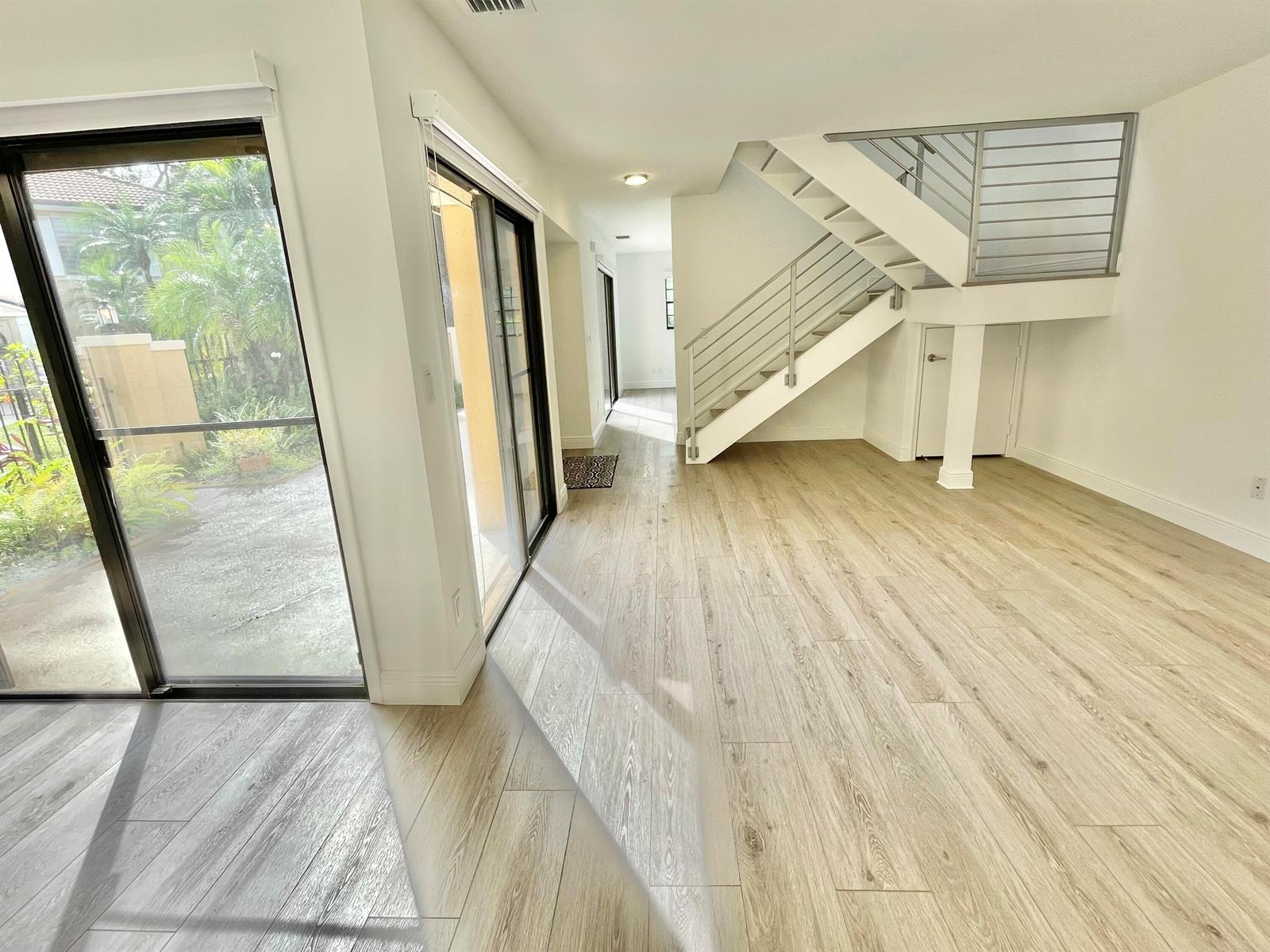 An interior view shows a room with light wood flooring, a staircase, and sliding glass doors — 359 Prestwick Circle # 2, Palm Beach Gardens FL 33418, PALM BEACH GARDENS, FL
