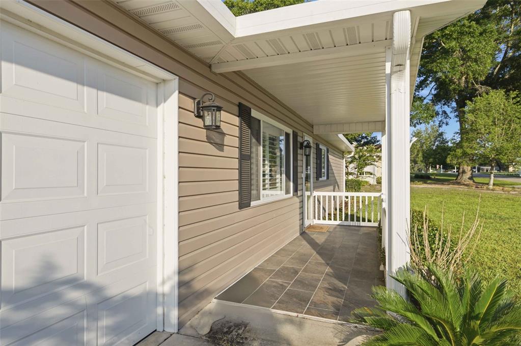 A covered porch with tiled flooring runs alongside a house with beige siding and shutters — 6274 SW 106TH PLACE, OCALA, FL