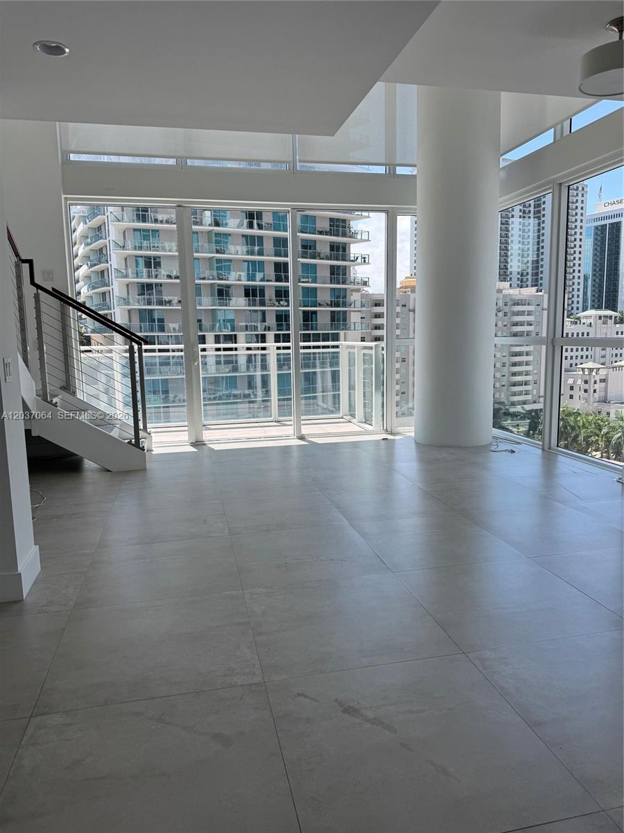 An empty room with large windows, tile flooring, a central pillar, and an interior staircase — 1080 Brickell Ave # 1101, Miami FL 33131, MIAMI, FL