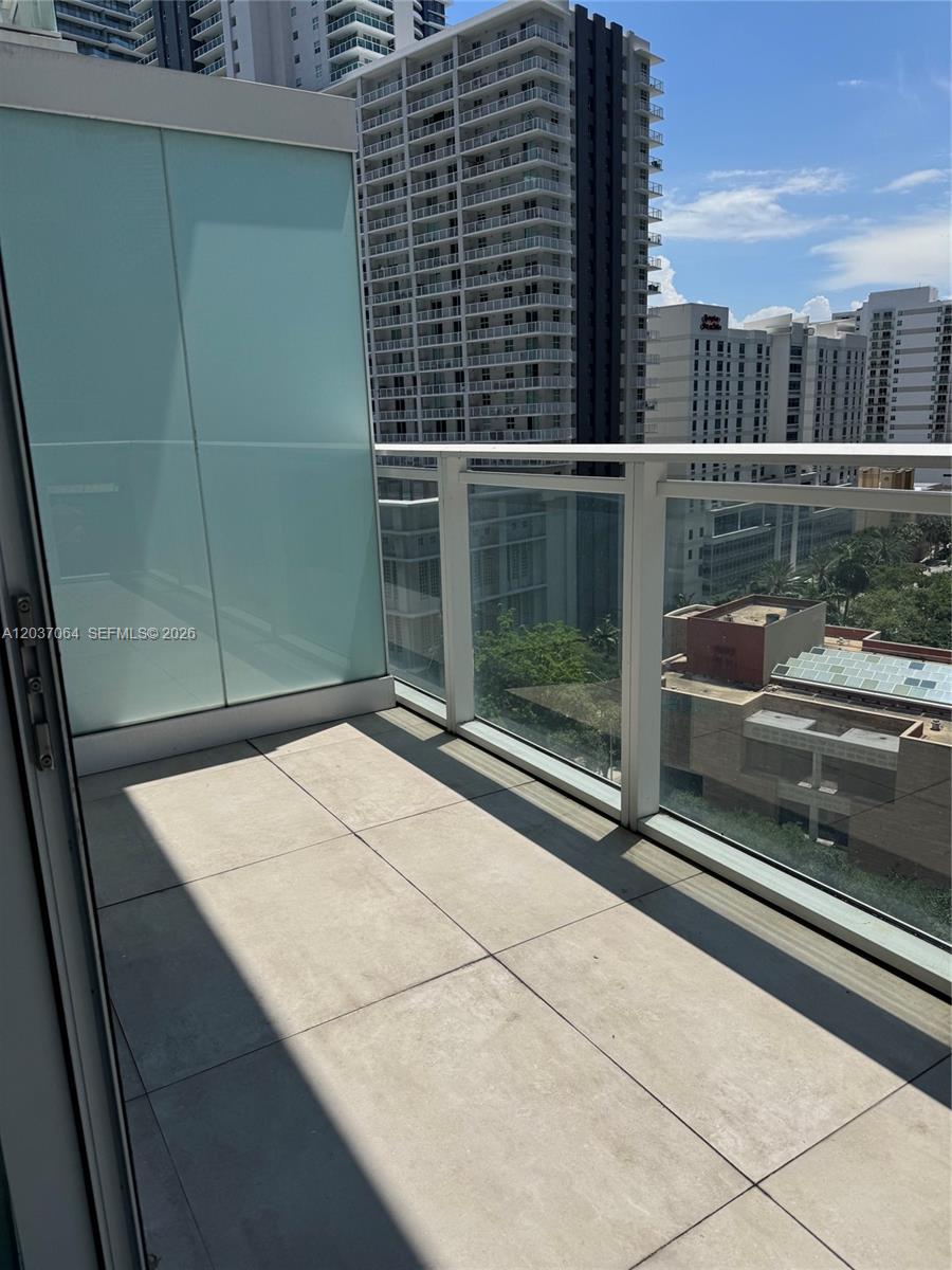 A balcony with light-colored floor tiles, glass railings, and views of surrounding high-rise buildings — 1080 Brickell Ave # 1101, Miami FL 33131, MIAMI, FL