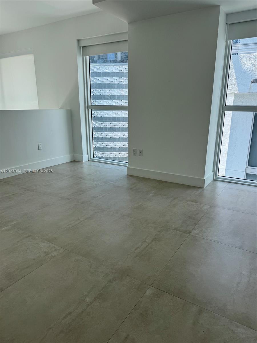 An empty room features large light-colored floor tiles, white walls, and two tall windows — 1080 Brickell Ave # 1101, Miami FL 33131, MIAMI, FL