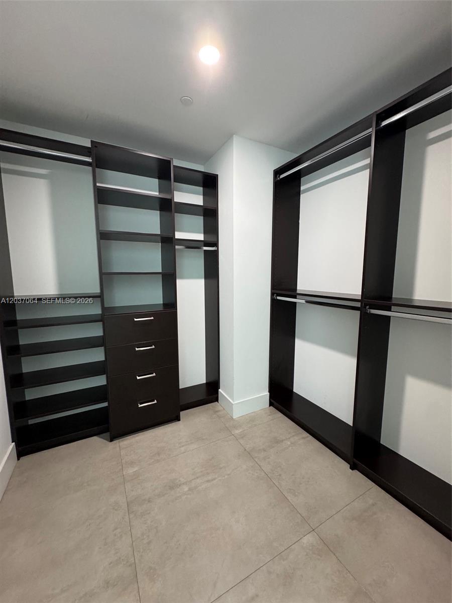 A walk-in closet features dark wood shelving, hanging rods, and light-colored tile flooring — 1080 Brickell Ave # 1101, Miami FL 33131, MIAMI, FL