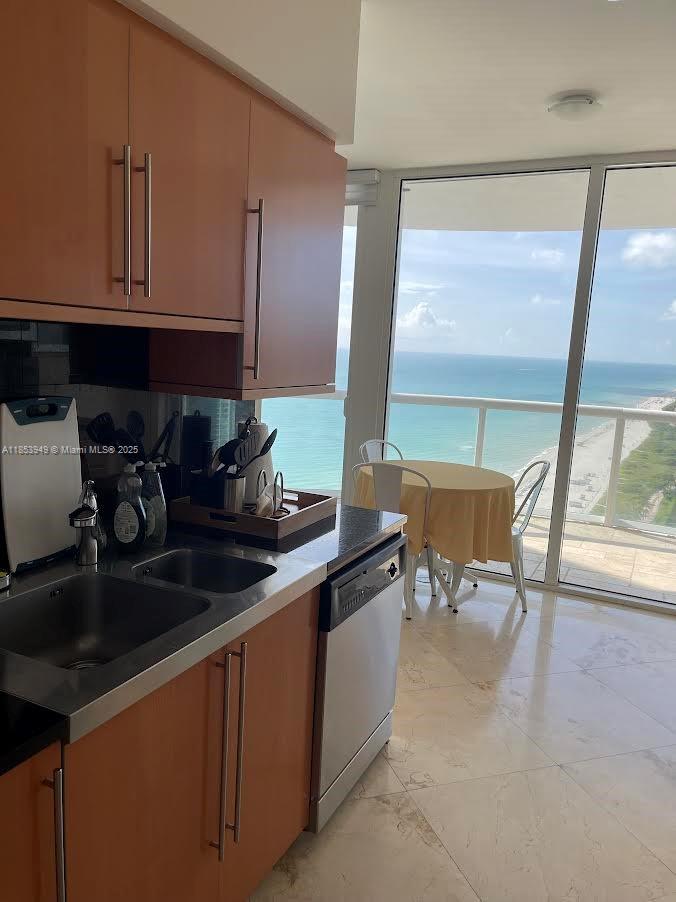 A kitchen with wood cabinets and a stainless steel dishwasher overlooks a balcony and ocean — 6365 Collins Ave # 3404, Miami Beach FL 33141, MIAMI BEACH, FL
