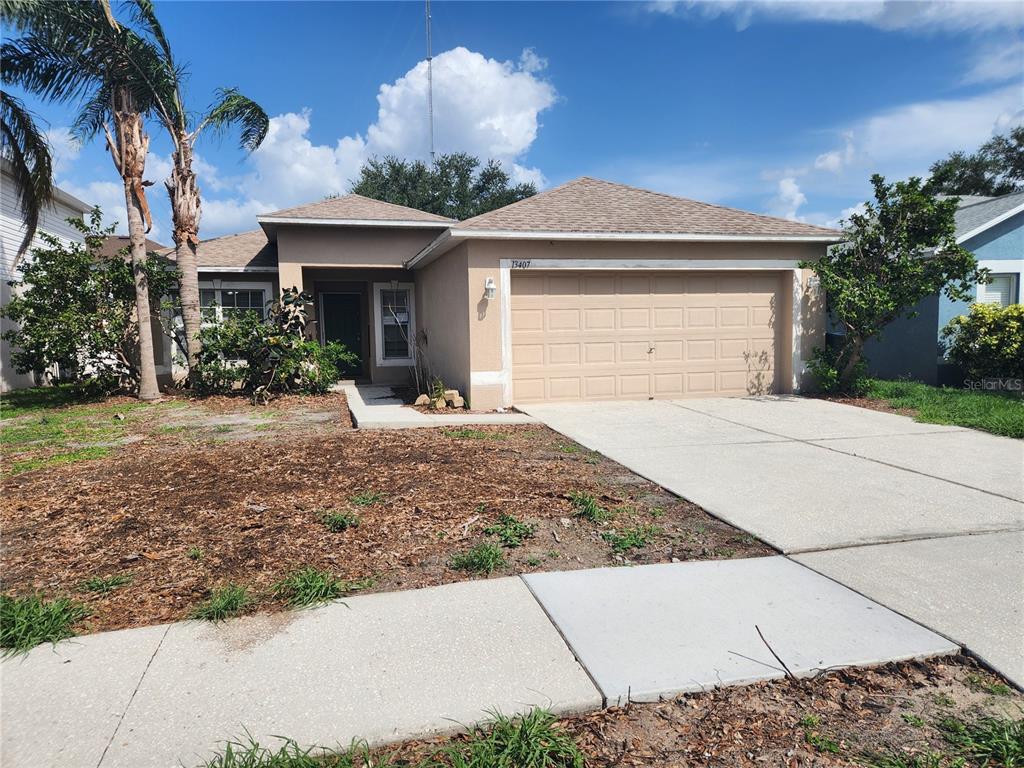 A single-story tan stucco house features a two-car garage and a front walkway — 13407 COPPER HEAD DRIVE, RIVERVIEW, FL