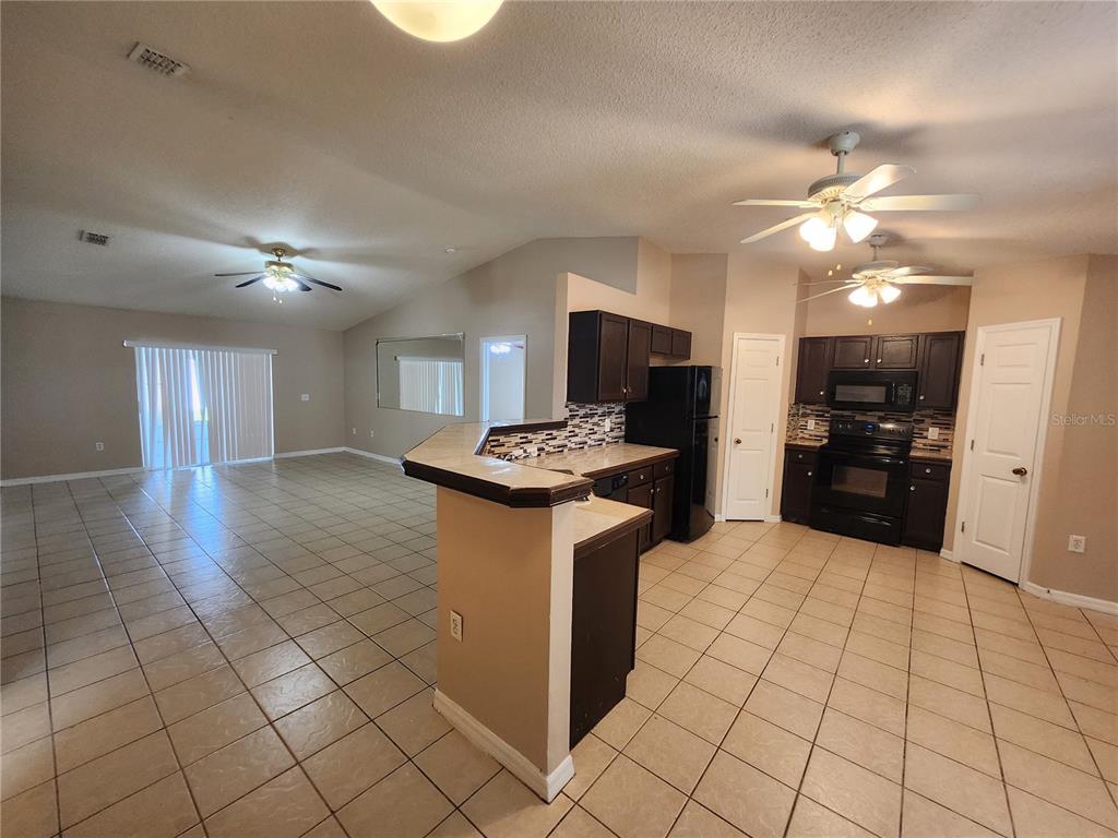 An open-concept kitchen and living area features tile flooring, dark cabinetry, and two ceiling fans — 13407 COPPER HEAD DRIVE, RIVERVIEW, FL
