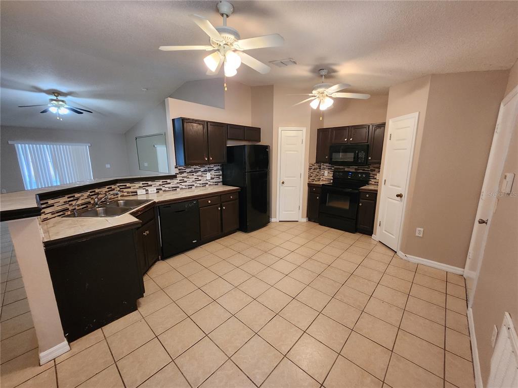 A kitchen with dark cabinets, black appliances, tile flooring, and a tiled backsplash — 13407 COPPER HEAD DRIVE, RIVERVIEW, FL