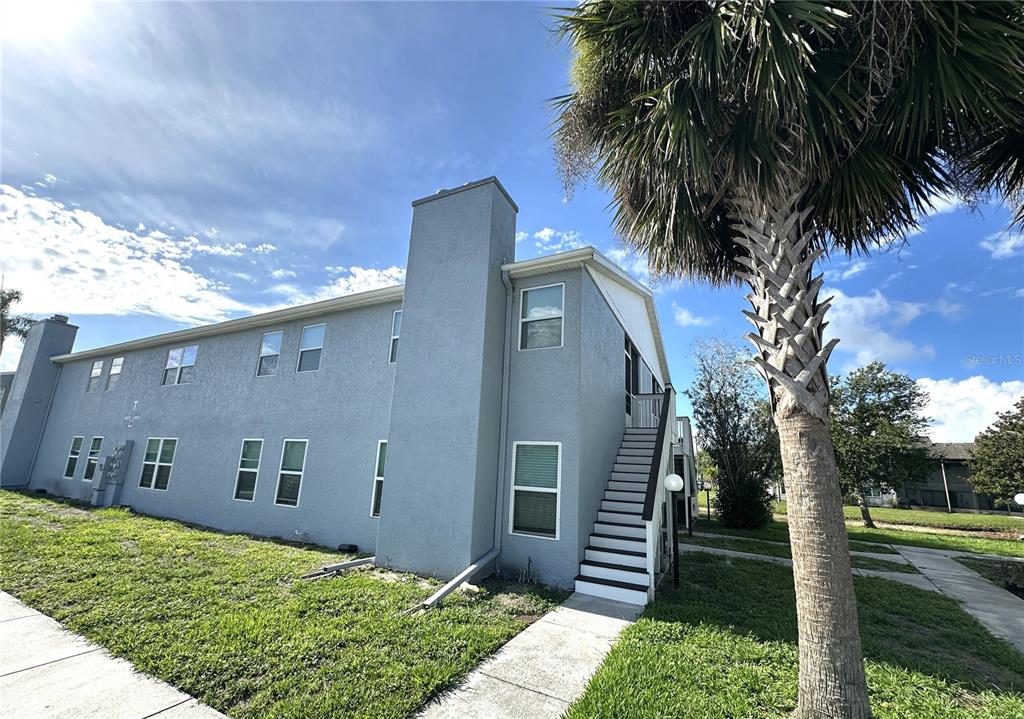 A two-story gray stucco apartment building features a staircase leading to an upper-level entrance — 3821 59TH AVENUE W UNIT 3821, BRADENTON, FL