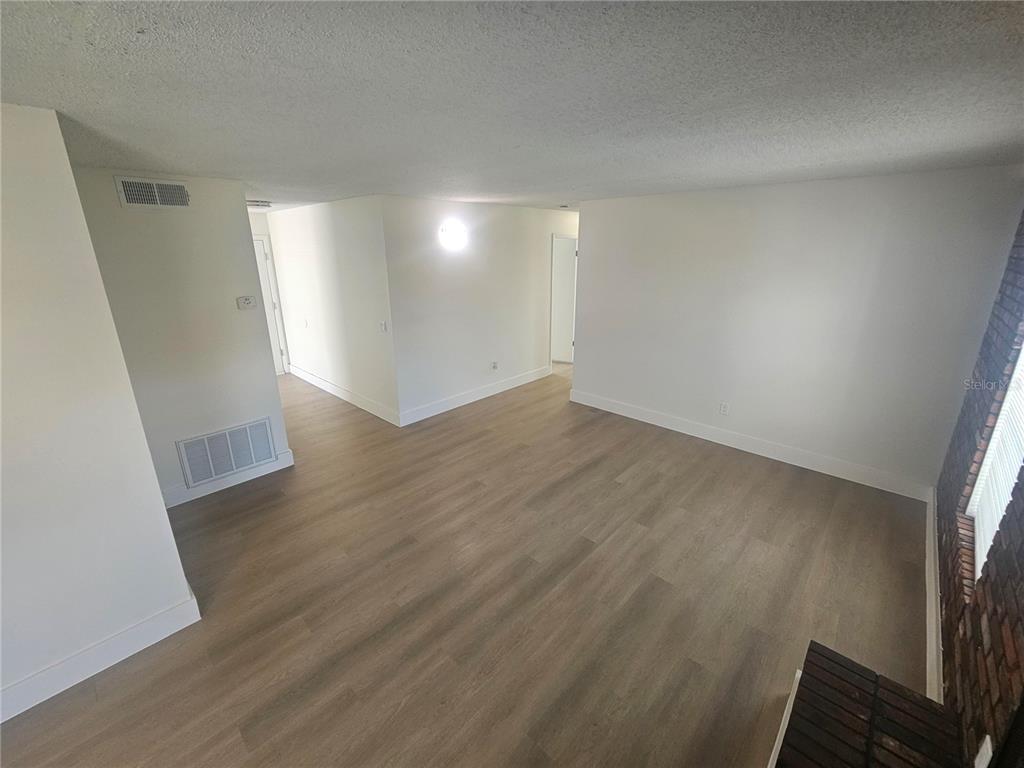 An empty living room features light wood-look flooring, white walls, and a brick accent wall — 372 IMPERIAL DRIVE, CASSELBERRY, FL