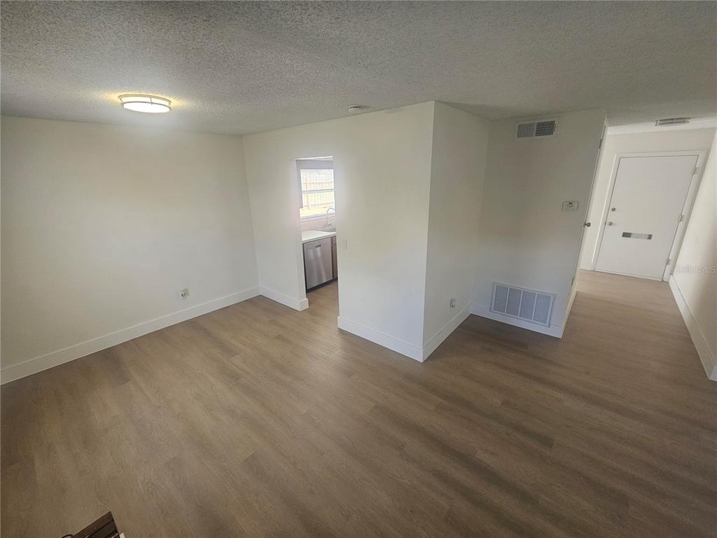 An empty room with light wood-look flooring and a doorway leading to a kitchen — 372 IMPERIAL DRIVE, CASSELBERRY, FL