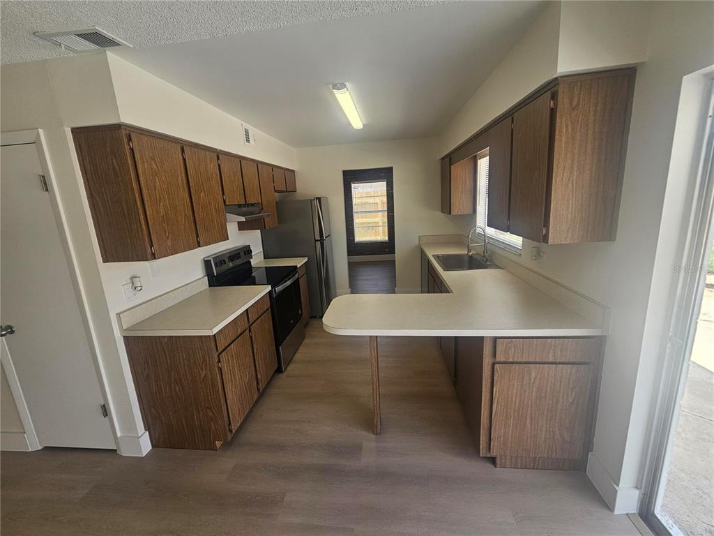 A kitchen features wood cabinets, light countertops, stainless steel appliances, and light wood-look flooring — 372 IMPERIAL DRIVE, CASSELBERRY, FL