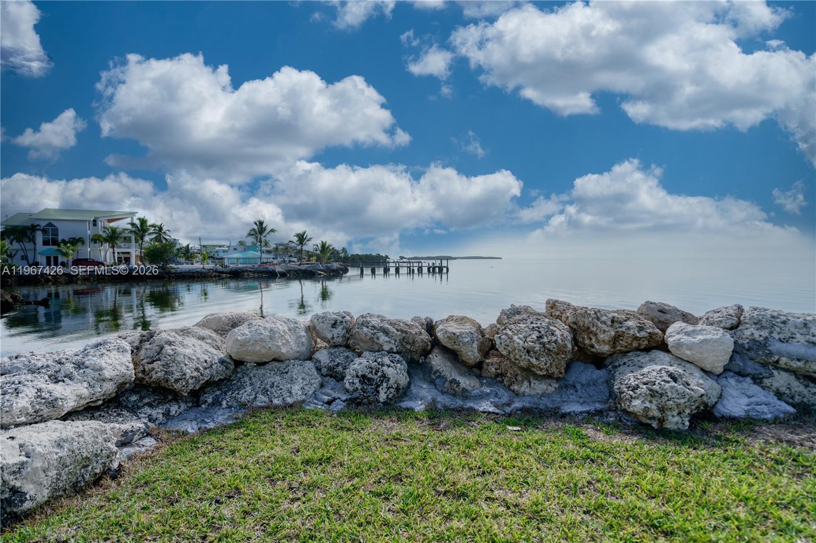 A stone seawall borders a grassy lawn overlooking a calm bay with a wooden dock — 94825 Overseas #178 # 178, Key Largo FL 33037, KEY LARGO, FL