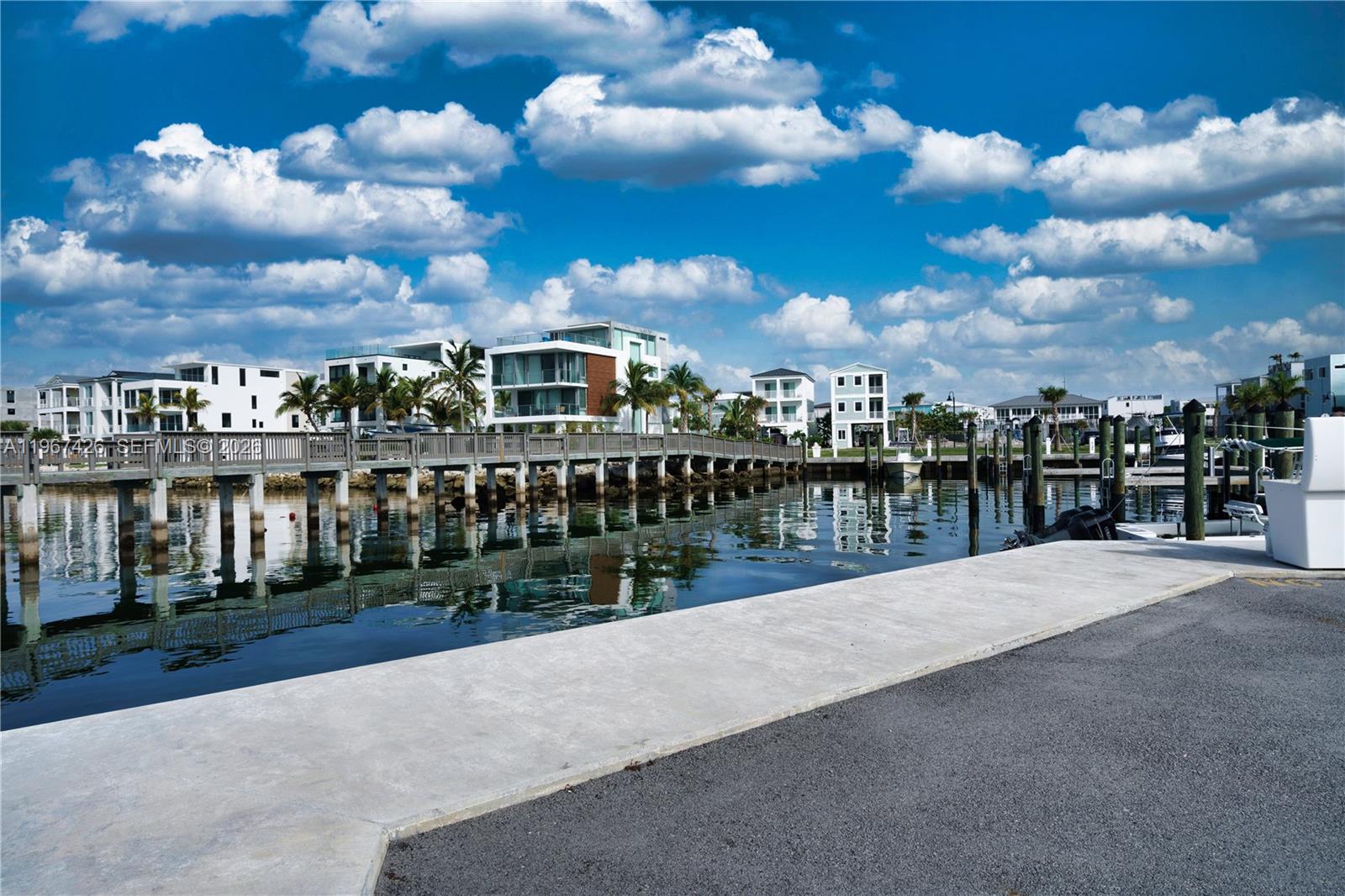 A concrete dock overlooks a calm waterway with modern waterfront homes and a wooden bridge — 94825 Overseas #178 # 178, Key Largo FL 33037, KEY LARGO, FL