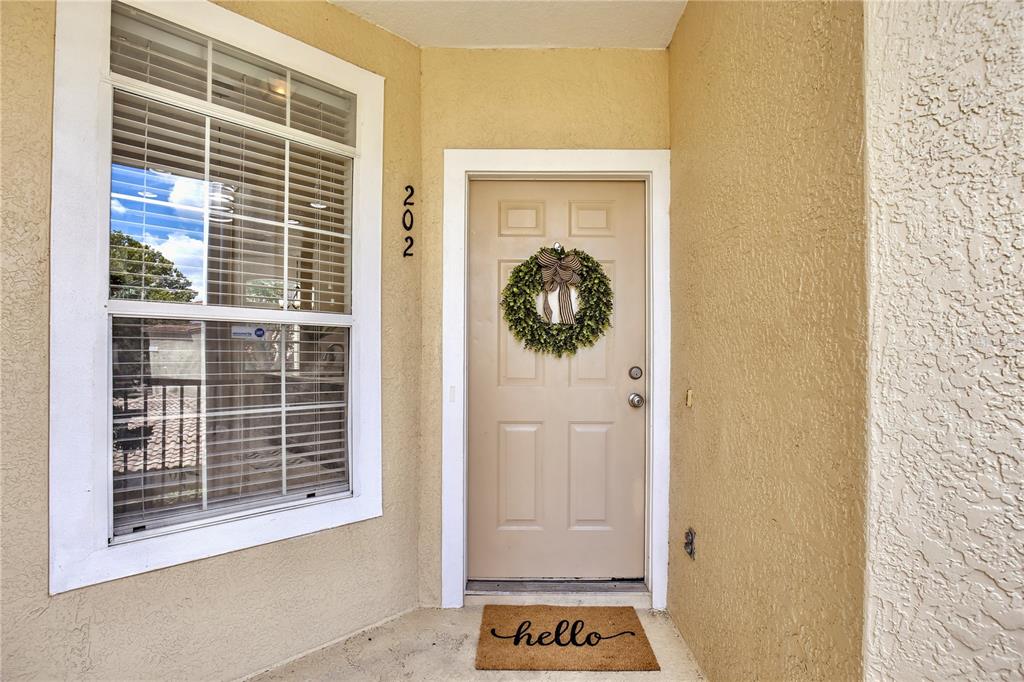 A tan front door with a wreath and a hello doormat sits beside a window — 696 SEABROOK COURT UNIT 202, ALTAMONTE SPRINGS, FL