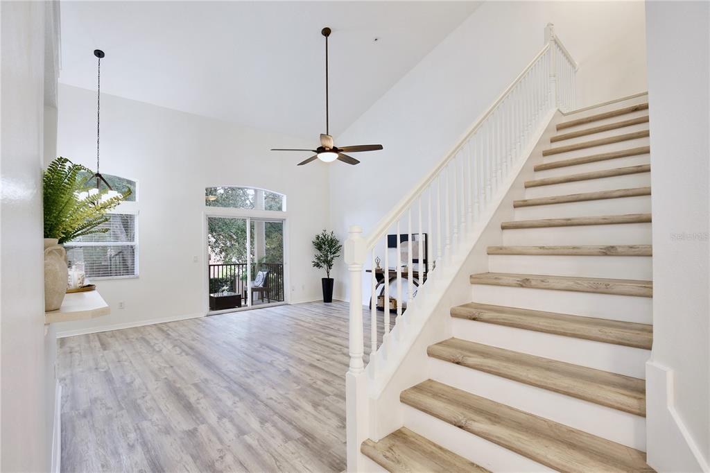 A bright living room features light wood-look flooring, a high ceiling, and a wooden staircase — 696 SEABROOK COURT UNIT 202, ALTAMONTE SPRINGS, FL